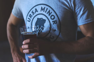 Man standing holding pint glass with Ursa Minor shirt